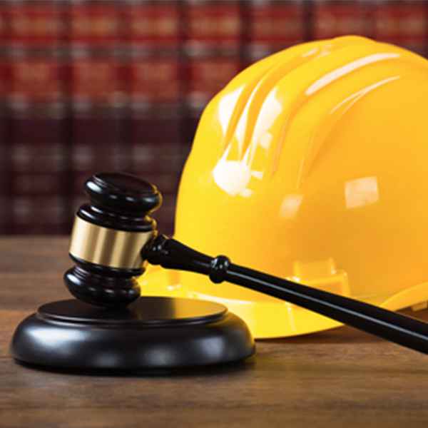 A yellow construction helmet placed next to a judge’s gavel on a wooden desk, symbolizing construction law or legal matters related to the construction industry.