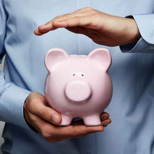 A person in a business suit holding and protecting a pink piggy bank, symbolizing financial security.